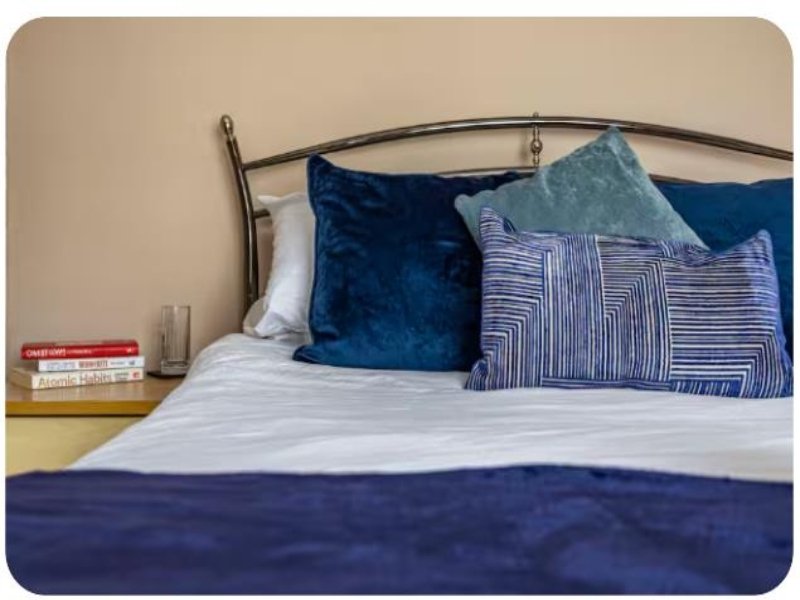 Bed with blue velvet pillows, striped cushion, white sheets and bedside table with books