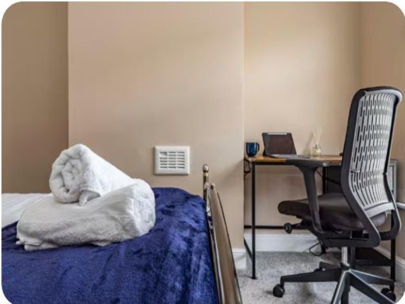 Bedroom with single bed, blue bedding, white towels, desk with office chair and laptop