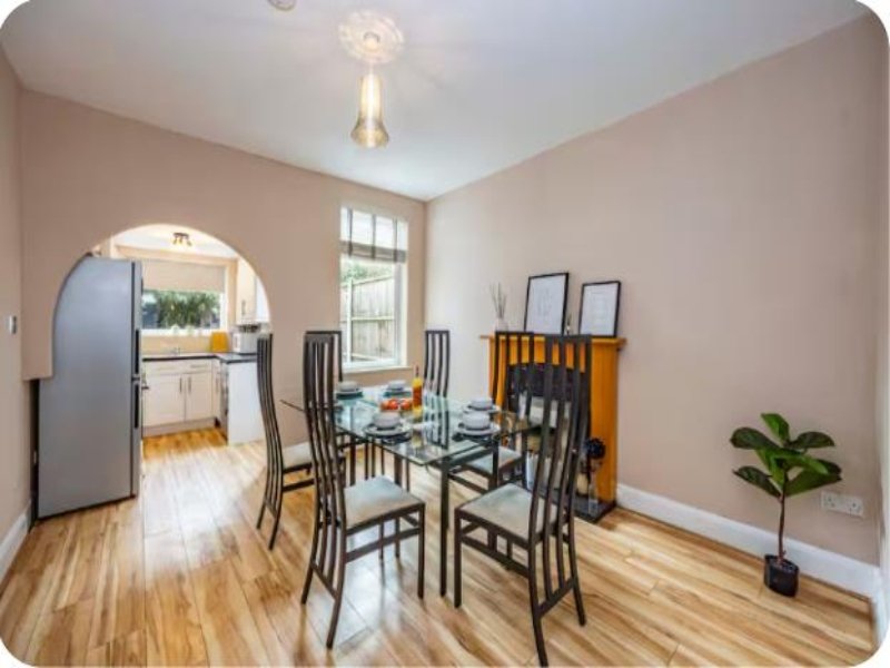 Dining room with glass table, black chairs, wooden floors and archway to kitchen
