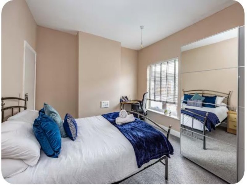 Bedroom with two metal-frame beds, white bedding, blue cushions and throws, and mirror