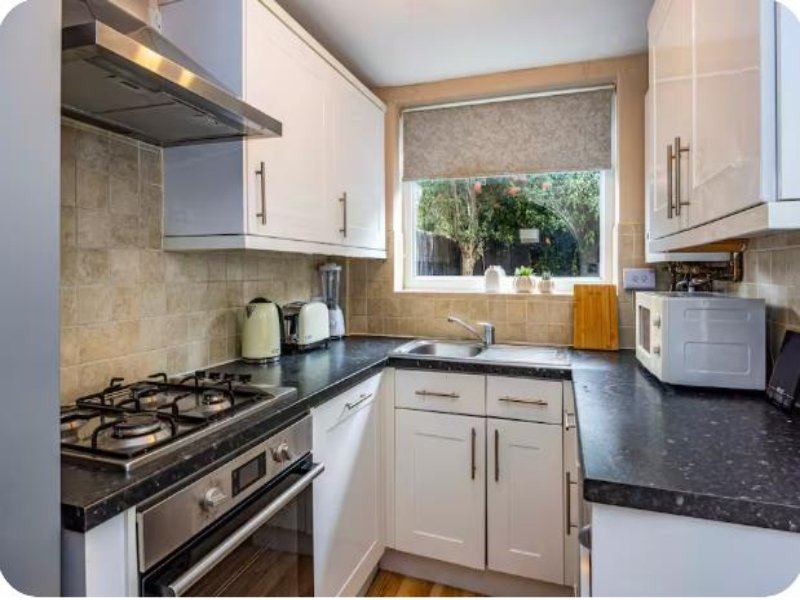 Modern kitchen with white cabinetry, black granite countertops, gas stove and window view