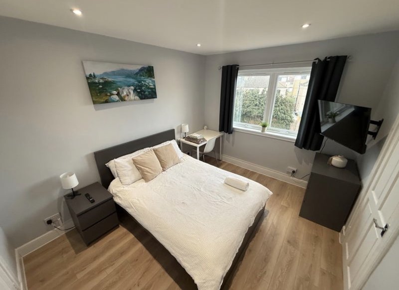 Modern bedroom with double bed, black headboard, wooden flooring, wall art and TV