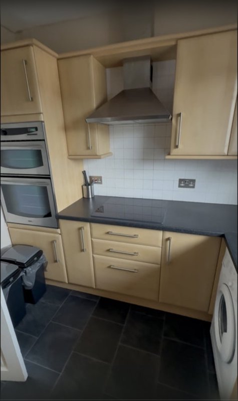 Kitchen with cream cabinets, black countertops, stainless steel extractor hood and built-in appliances