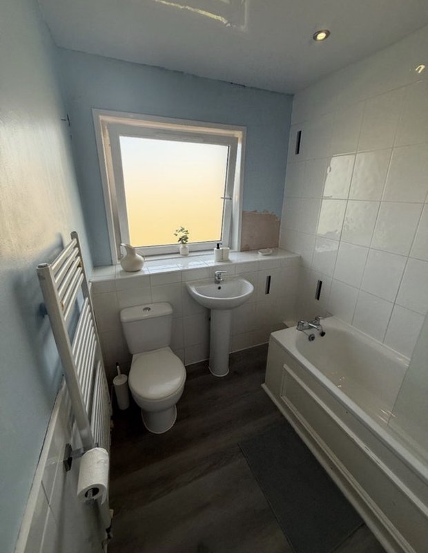 Modern bathroom with toilet, pedestal sink, bathtub and window with blue walls