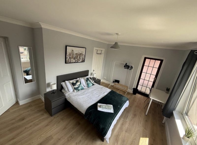 Spacious bedroom with double bed, wooden flooring, grey walls and multiple windows