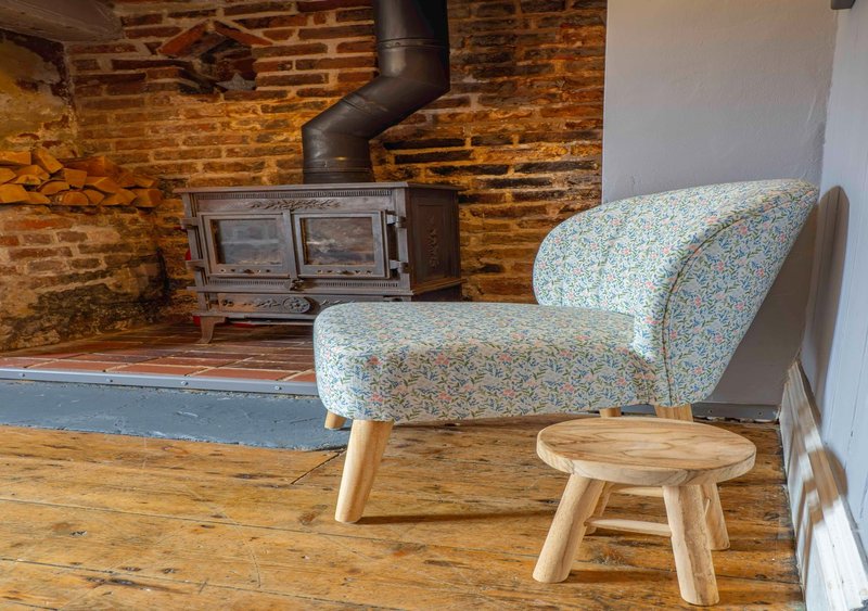 Industrial loft space with exposed brick, wood-burning stove, patterned armchair and wooden stool