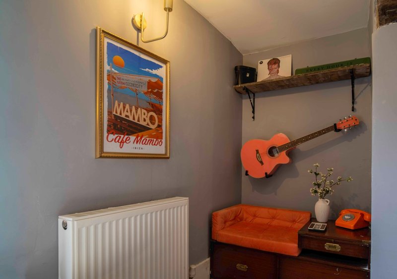Bedroom corner with orange acoustic guitar, radiator, framed vintage poster, and orange cushioned chair