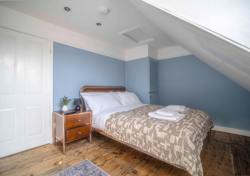 Attic bedroom with sloped ceiling, blue walls, wooden bed frame and hardwood flooring