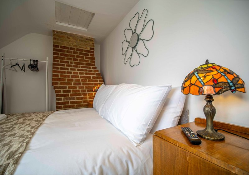 Bedroom with white bedding, exposed brick wall, wooden nightstand and orange stained-glass lamp