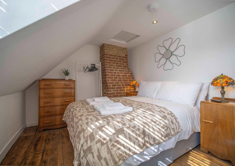 Attic bedroom with double bed, wooden furniture, brick chimney and wire wall art
