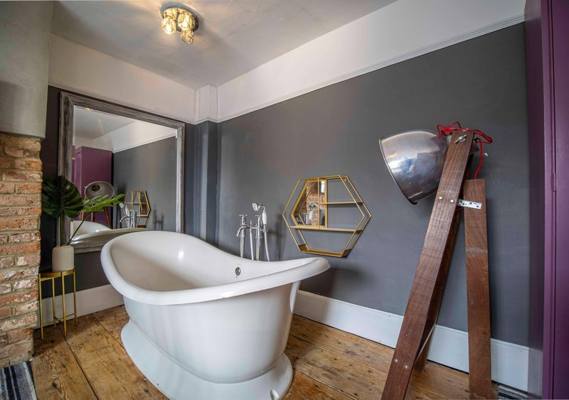 Modern bathroom with freestanding white bathtub, gray walls, wooden floor, and decorative mirror