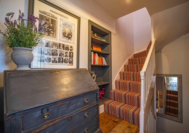 Hallway with wooden chest, striped staircase, framed photos and decorative vase with flowers
