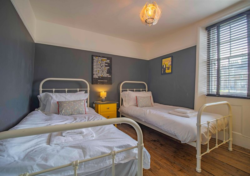 Bedroom with three single beds, metal frames, grey accent wall and wooden flooring