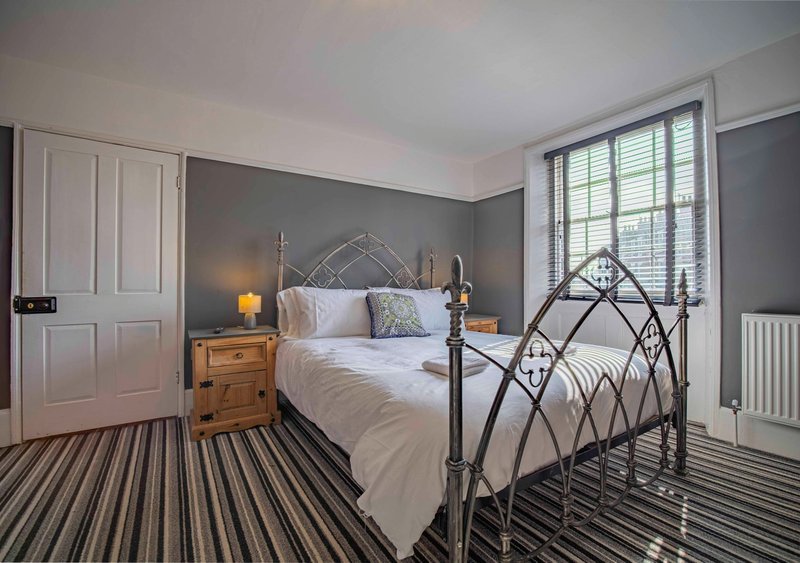 Bedroom with metal frame bed, wooden nightstand, striped carpet and shuttered window