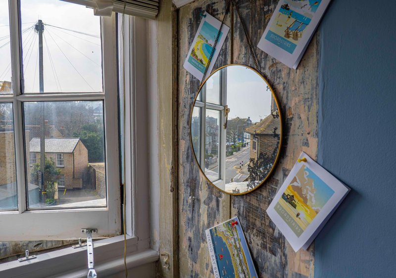 Bedroom wall with round mirror, framed prints, window overlooking residential street