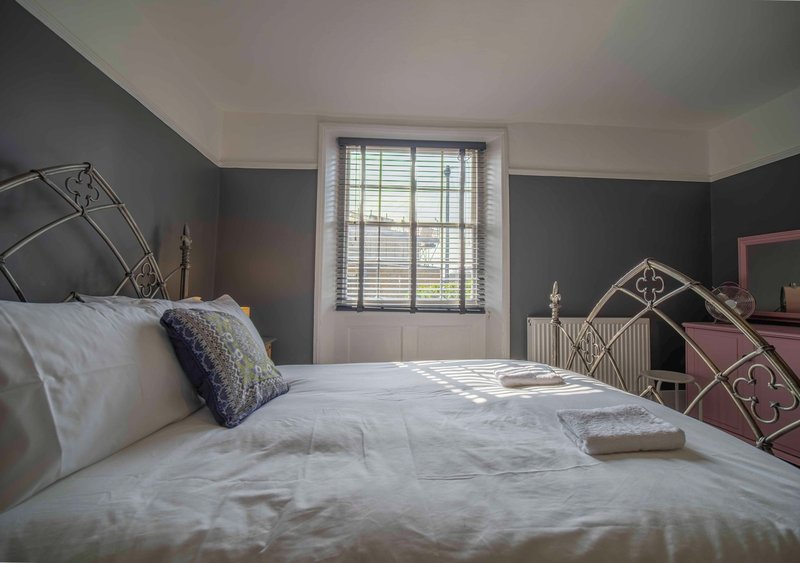 Bright bedroom with double bed, grey walls, window with shutters, and decorative bedding