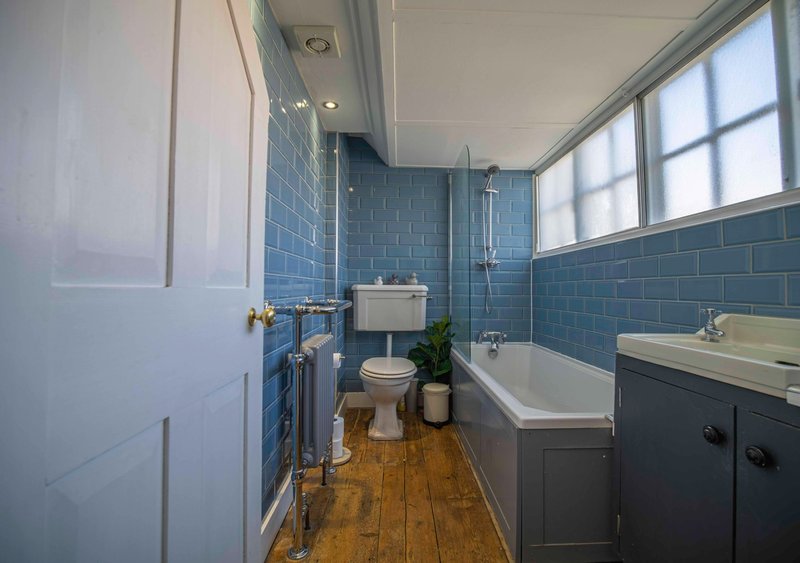 Modern bathroom with blue subway tiles, white bathtub, toilet, sink vanity and wooden flooring