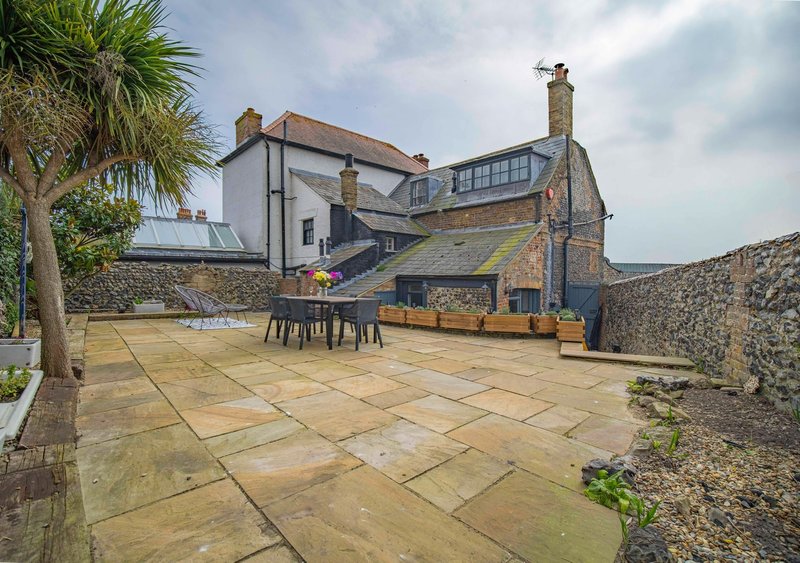 Spacious outdoor patio with stone terrace, dining table, palm tree and period property behind