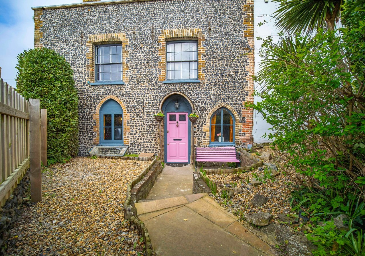 Stone cottage exterior with pink door, gravel driveway and climbing ivy