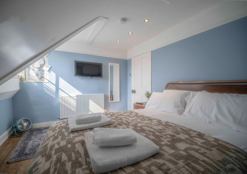 Bright attic bedroom with blue walls, wooden bed frame, white bedding and floor cushions
