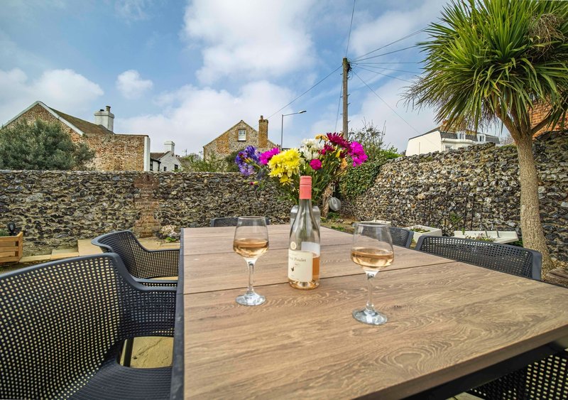 Outdoor terrace with wooden dining table, wicker chairs, wine glasses and flower arrangement