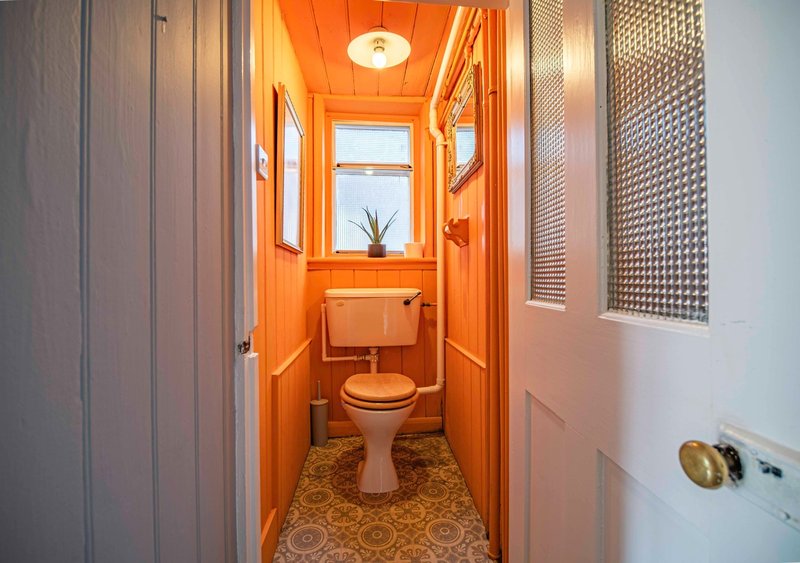 Narrow bathroom with orange walls, toilet, sink and small window with plant