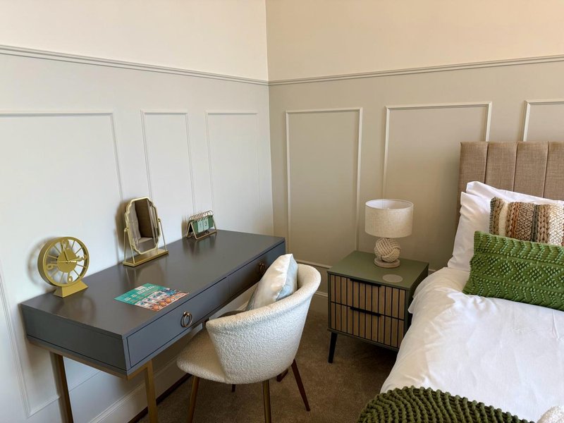 Modern bedroom with desk, chair, lamp, and bed with green accent pillow