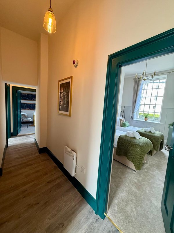 Hallway with teal-framed doorways, pendant light, and views into bedroom and kitchen