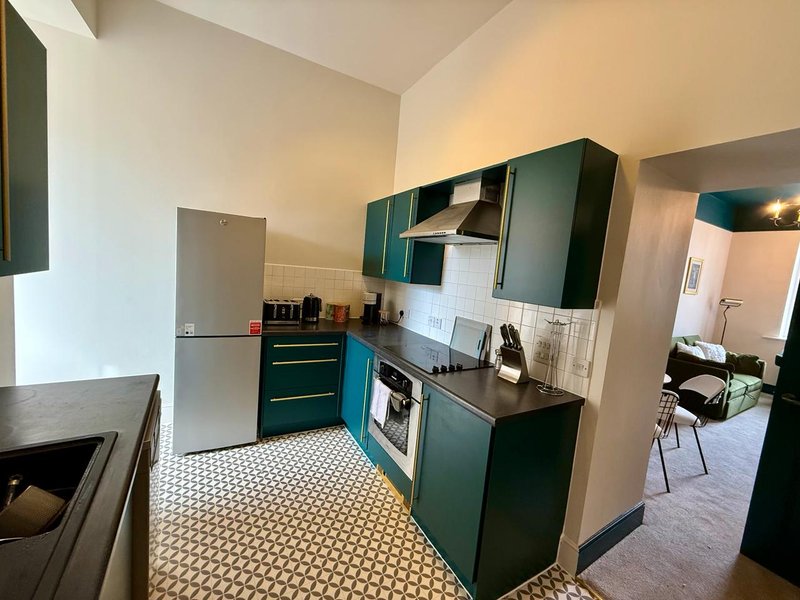 Modern kitchen with teal cabinetry, stainless steel appliances, and geometric floor tiles