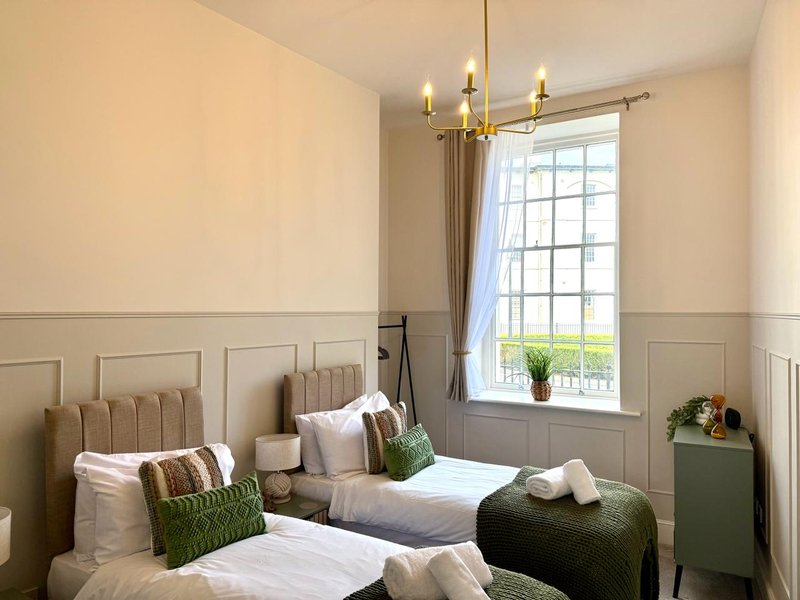 Twin bedroom with cream headboards, white bedding, green accents, and brass chandelier