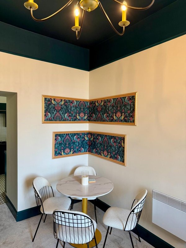 Dining nook with round table, modern chairs, framed tapestries, brass chandelier and cream walls