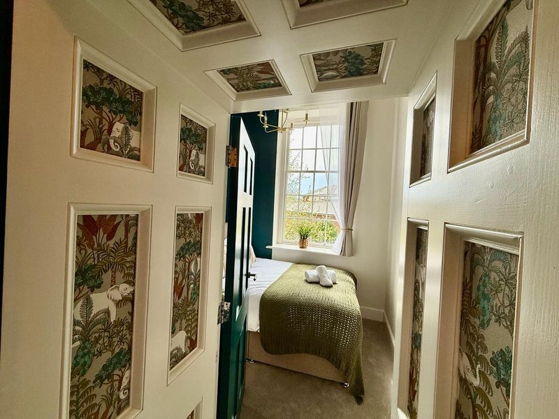 Narrow hallway with framed botanical prints on walls leading to bedroom with single bed