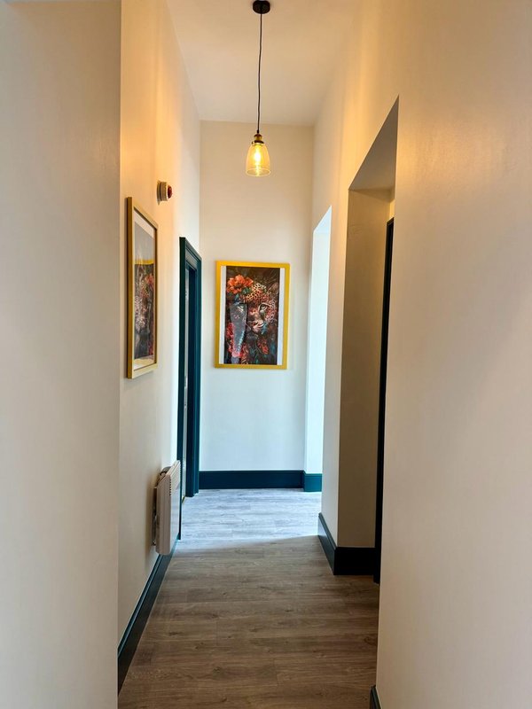 Narrow hallway with wooden floor, white walls, pendant light, and framed artwork