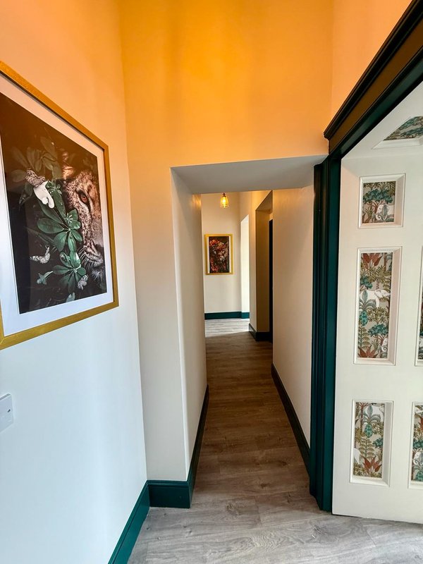 Narrow hallway with orange walls, wooden floor, framed botanical artwork and framed prints