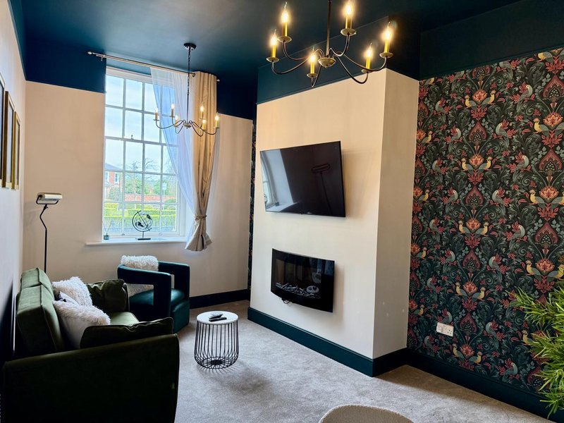 Modern living room with fireplace, wall-mounted TV, black sofa, chandelier, and floral accent wall