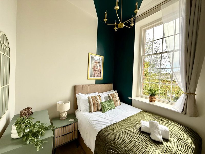 Bright bedroom with single bed, green accent wall, large window and potted plant