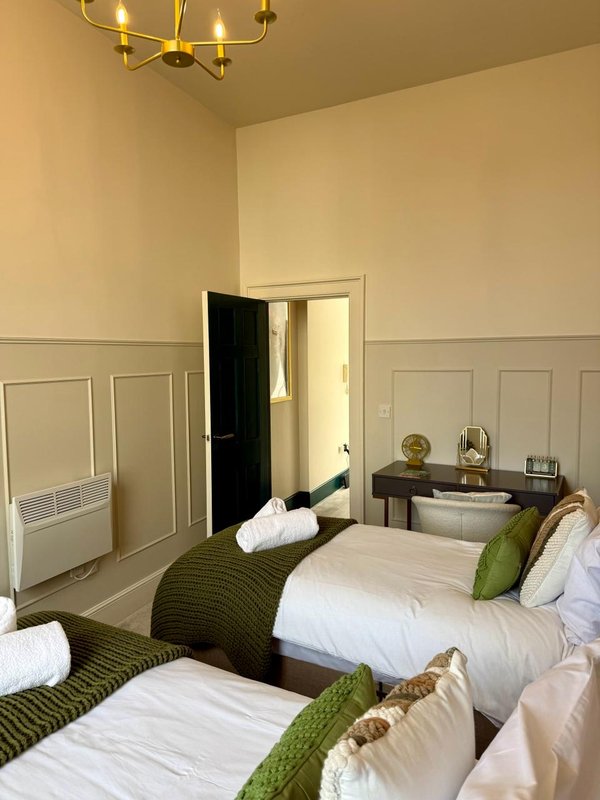Twin bedroom with two single beds, green throws, brass ceiling light and ensuite door