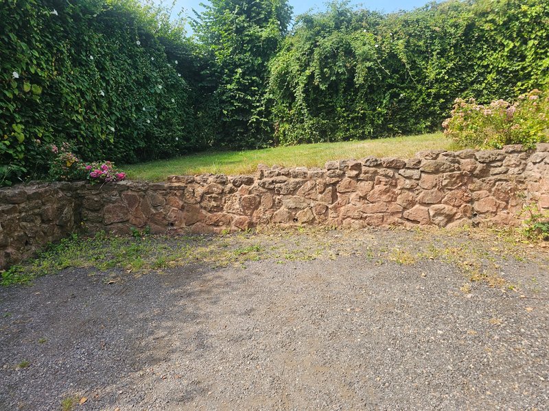 Property driveway with stone wall, green lawn and mature trees in background