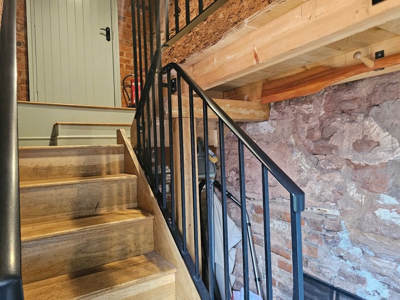 Interior staircase with wooden steps, black metal railing, exposed brick wall and wooden beam ceiling