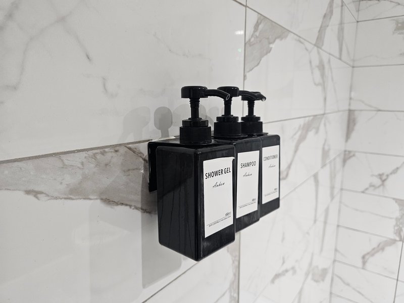 Bathroom wall-mounted dispenser with three black pump bottles on marble tile