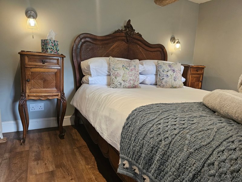 Traditional bedroom with ornate wooden bed, white pillows, patterned cushions, bedside tables and wall lamps
