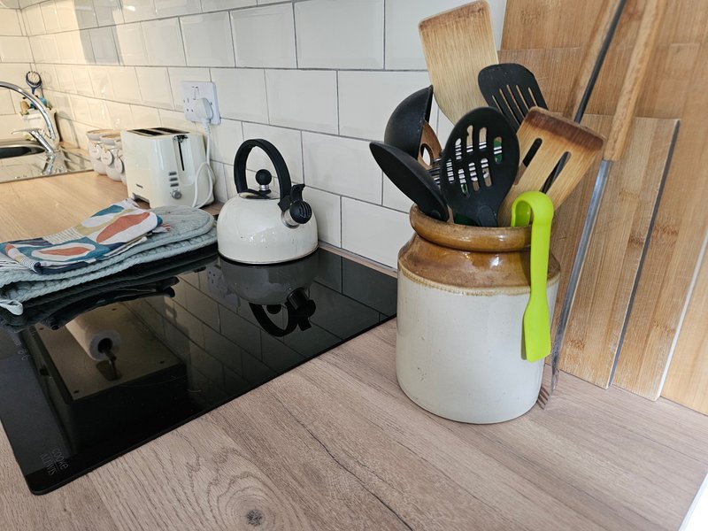 Kitchen countertop with white kettle, cooking utensils in ceramic holder, and induction hob