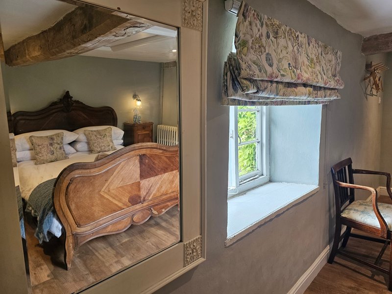 Bedroom with wooden bed, mirror, window seat, and period furnishings