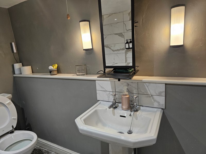 Modern bathroom with gray walls, pedestal sink, mirror and wall-mounted lighting fixtures