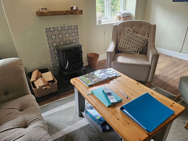Living room with upholstered armchairs, wood coffee table, black wood-burning stove and window