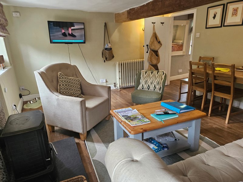 Open-plan living area with upholstered armchair, wooden table, sofa, and wooden dining chairs