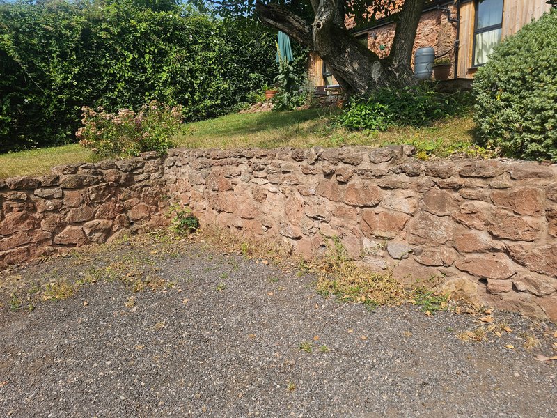 Property exterior showing stone retaining wall, driveway, brick building and mature trees