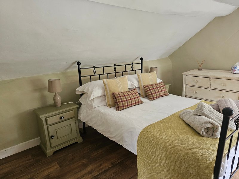 Bedroom with black metal bed frame, white bedding, plaid pillows, cream nightstand and wooden floor