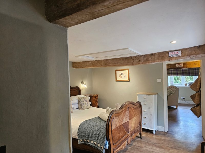 Bedroom with wooden bed frame, white cabinet, exposed beam ceiling, and doorway to adjacent room