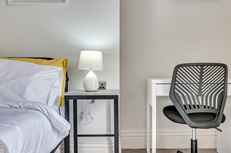 Bedroom with double bed, yellow throw, bedside table, lamp and black office chair